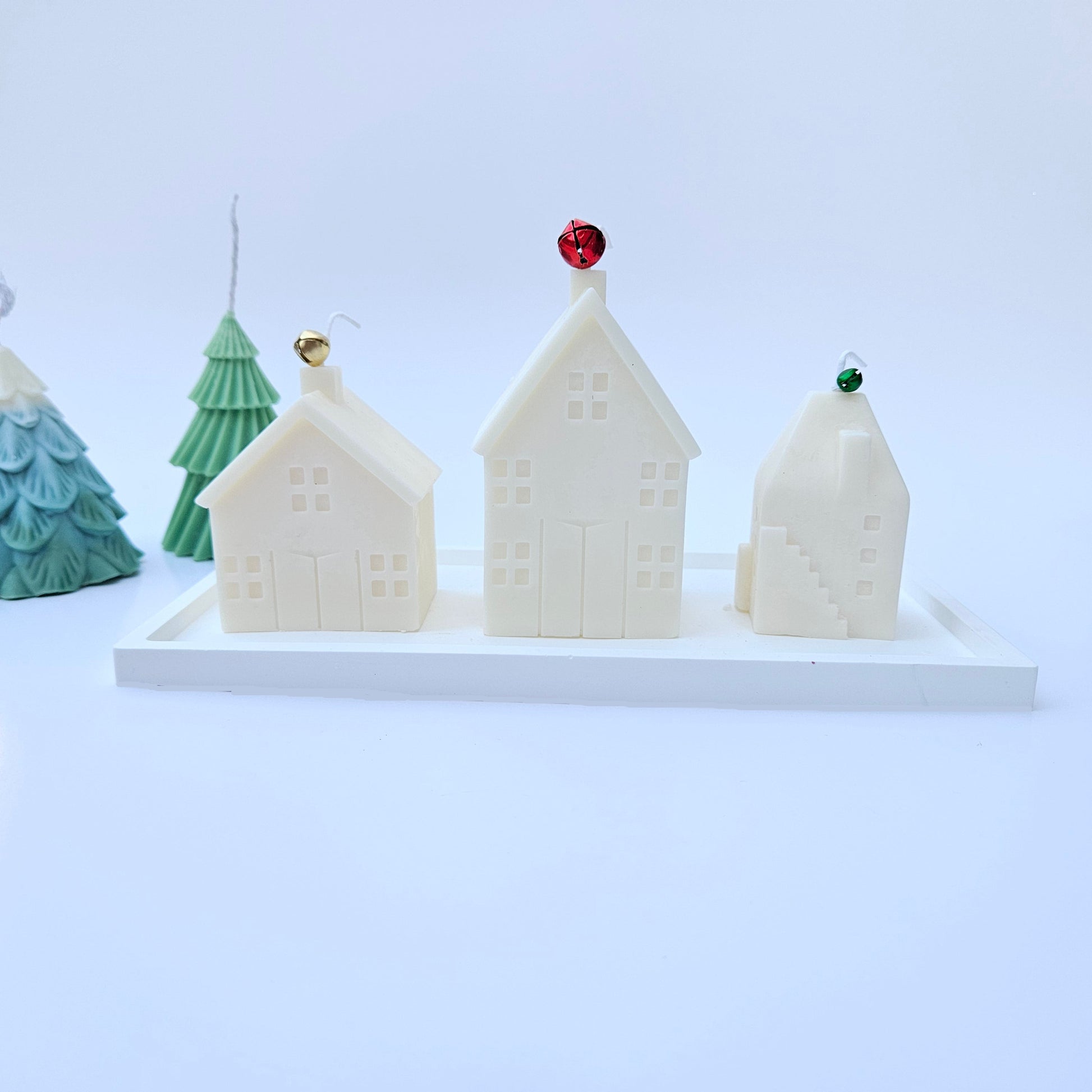 Decorative house-shaped candles on a white resin tray.